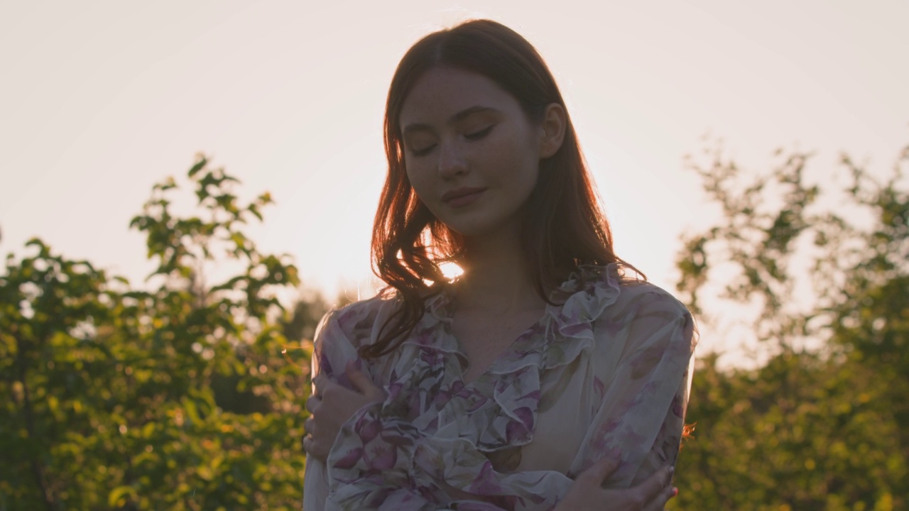 美丽的年轻女孩模特在夕阳的光束在国家，拥抱自己。自然美景。手持视频视频素材