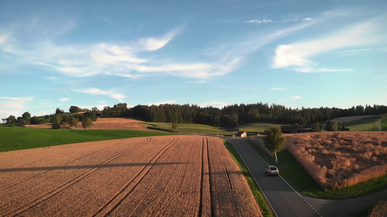 在金色的夕阳下，汽车行驶在空旷的柏油路上，穿过田野和草地。运输和农业综合企业的概念。耕地在傍晚夕阳的灯光下视频素材