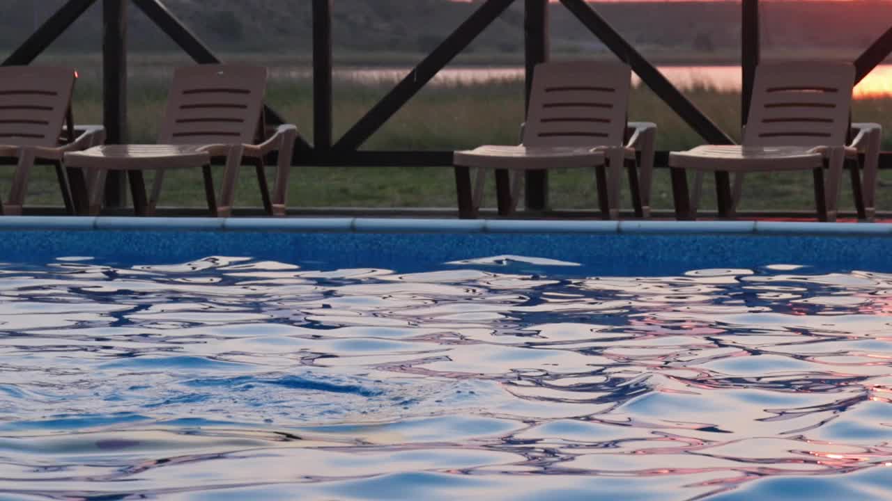 在夏日夕阳的映衬下，身穿彩色比基尼、头发湿漉漉的女孩从清澈透明的泳池里出来视频素材