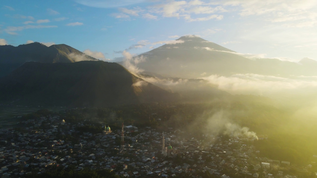 雾蒙蒙的村庄和稻田，龙目岛的背景是雄伟的林贾尼火山，位于森巴伦村。4 k鸟瞰图视频素材