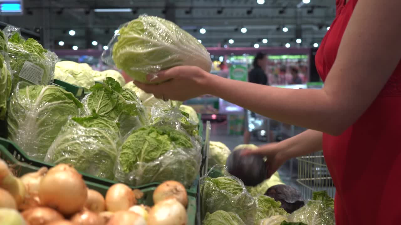 一个美丽的女人推着篮子从超市的货架上取下水果。在杂货店买食物。视频素材