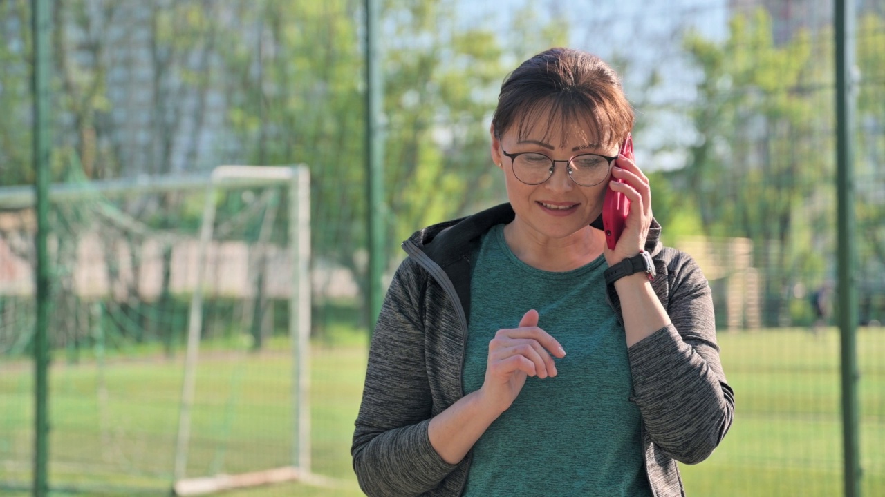 穿着运动服的中年妇女在电话中交谈，户外足球场体育场背景视频素材