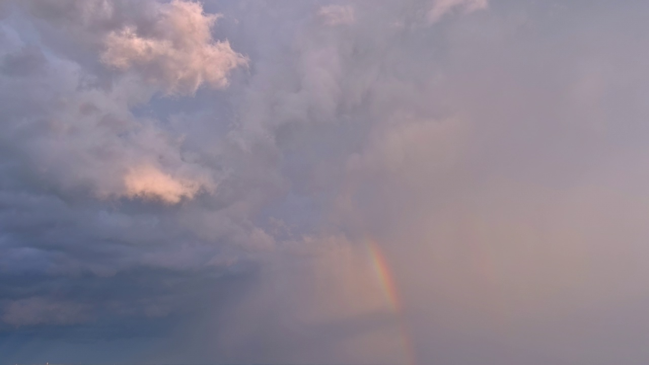 在暴风雨的天空中，一道明亮的彩虹映衬着云层视频素材