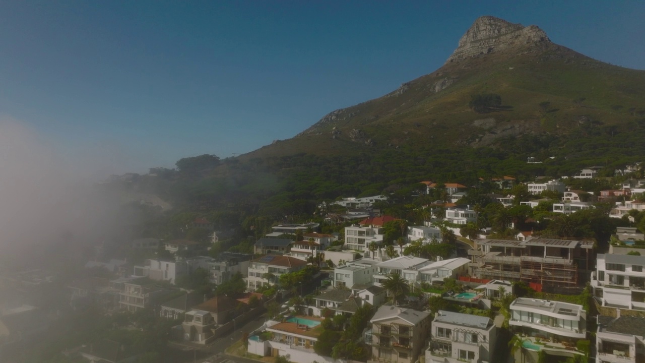 在旅游目的地的居民区上空飞行。前面是高高的岩石山峰。晨雾从海上升起。开普敦，南非视频素材