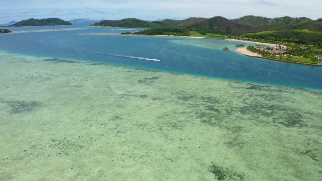 空中平移拍摄的快艇移动在海上由岛屿对多云的天空-苏瓦，斐济视频素材