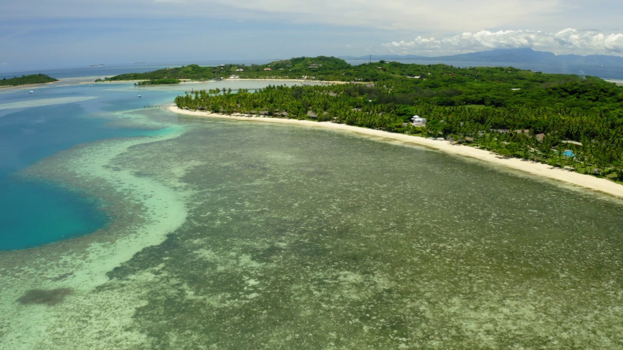 空中摇摄在岛上的绿树中拍摄的度假村，无人机飞越绿松石海-苏瓦，斐济视频素材