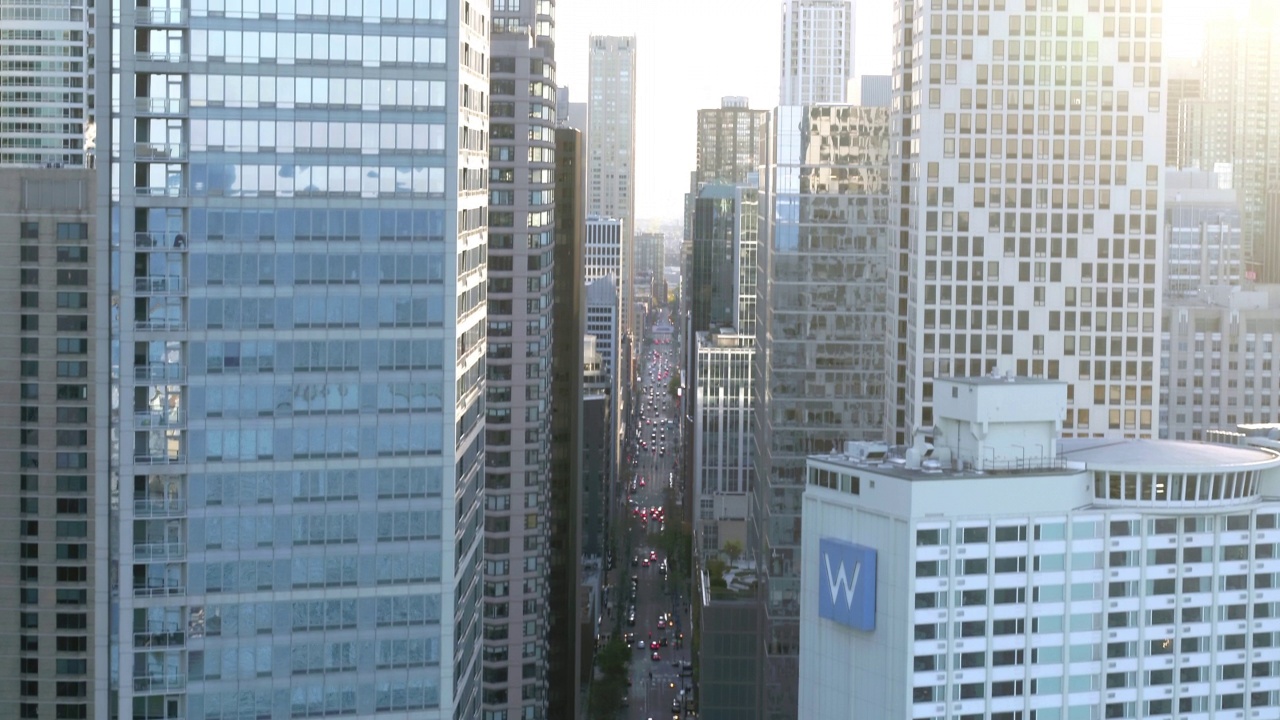 空中倾斜镜头的汽车移动在道路上的现代建筑对城市晴朗的天空-芝加哥，伊利诺伊州视频素材