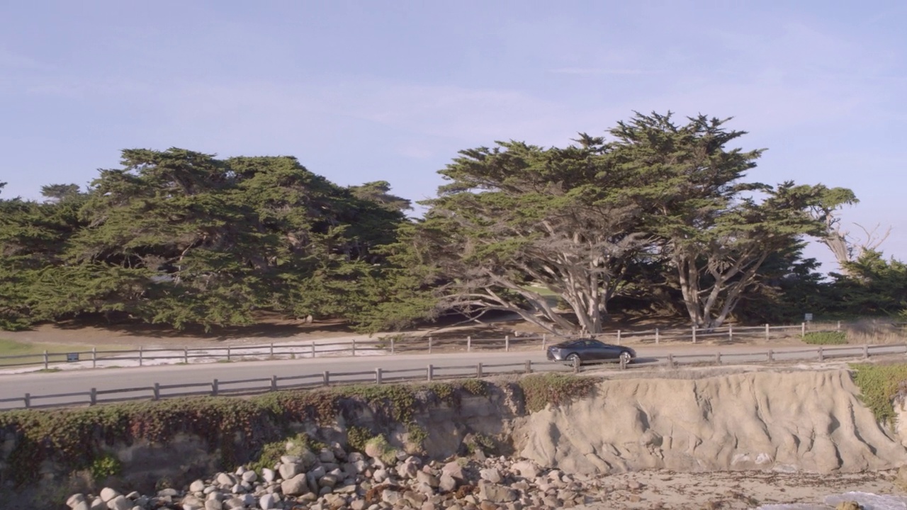 空中:车辆移动在道路上的绿色树木，无人机飞行向前在海上的波浪-德尔蒙特森林，加利福尼亚州视频素材