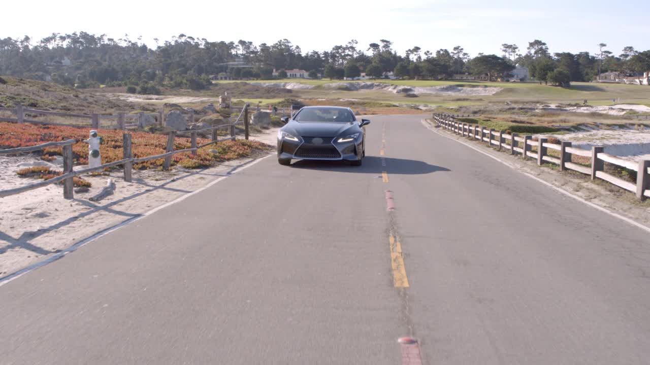 空中:黑色汽车移动在道路上海浪的海洋，无人机在阳光灿烂的日子向后飞行-德尔蒙特森林，加利福尼亚州视频素材