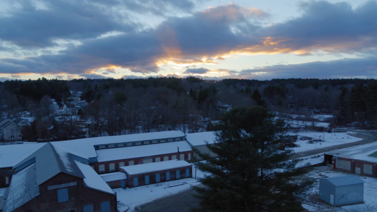 在夕阳西下的多云天空下，住宅城镇被雪覆盖的房子的向后航拍-奥兰治，马萨诸塞州视频素材