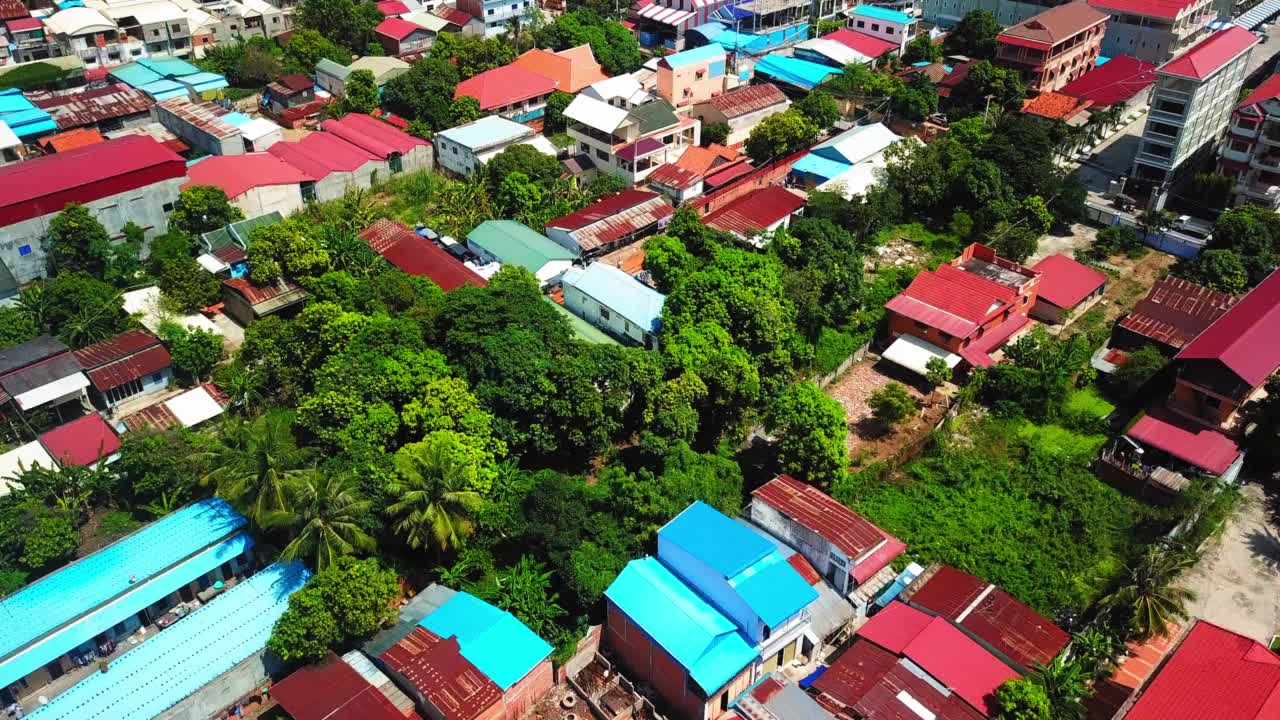 空中前进拍摄的住宅在绿色的树木在城市河边在阳光明媚的日子-金边，柬埔寨视频素材