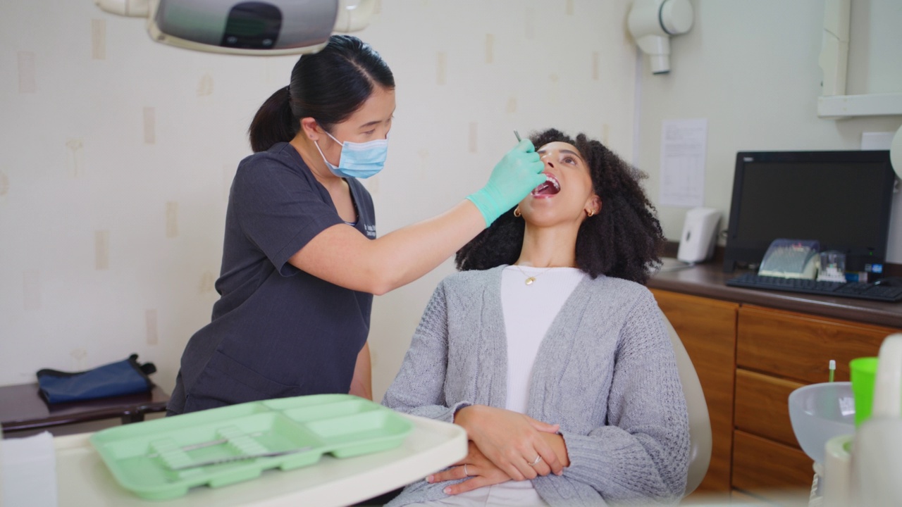 牙科医生在预约时用镜子工具检查女性病人的牙齿，并戴上口罩。非洲妇女进行例行检查，以预防蛀牙和牙龈疾病，并保持良好的口腔卫生视频素材