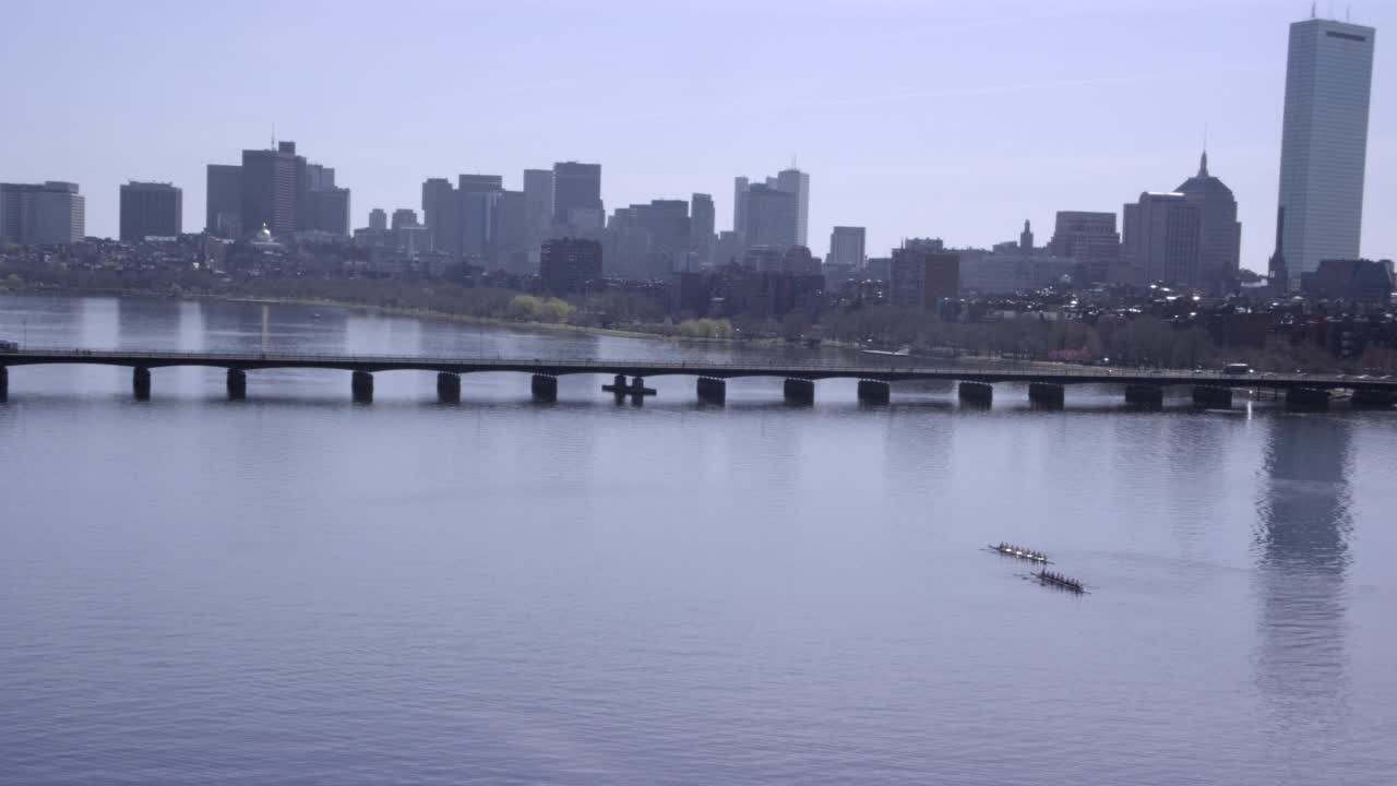 在波士顿市中心和金融中心附近的查尔斯河上空飞行。飞过赛艇队的划艇队员，然后在镜头结束时看到桥或堤道和城市天际线的一部分视频素材