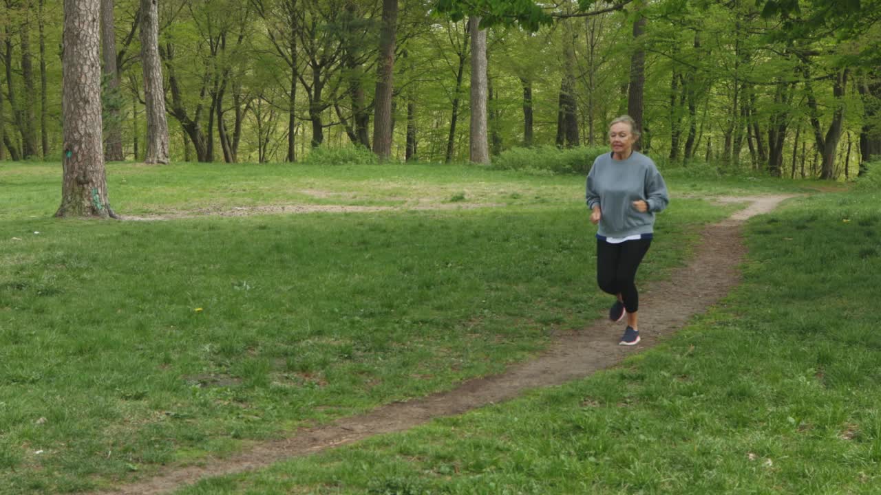 老年女子在绿色自然公园跑步，老年女子慢跑视频素材