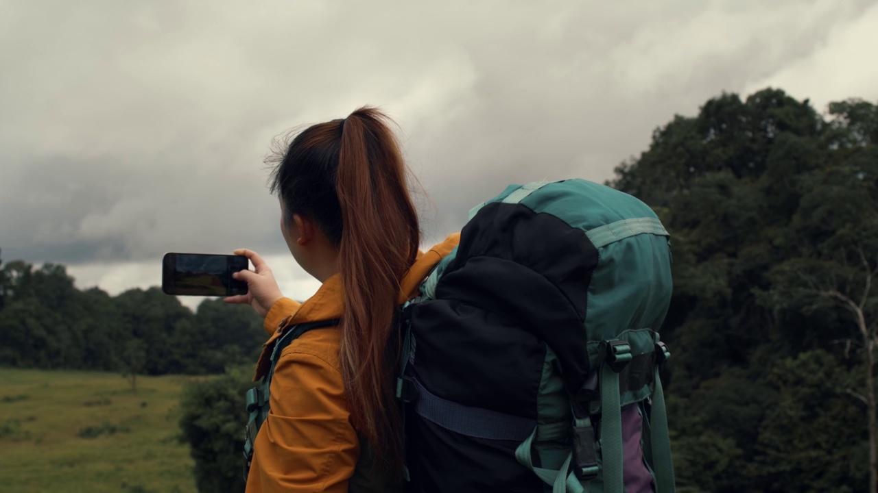 泰国森林徒步旅行的年轻女子。背着背包的活跃健康的女人。女性旅行者与漫步森林后视图，休闲，生物旅游，徒步旅行。她正在拍照。视频下载