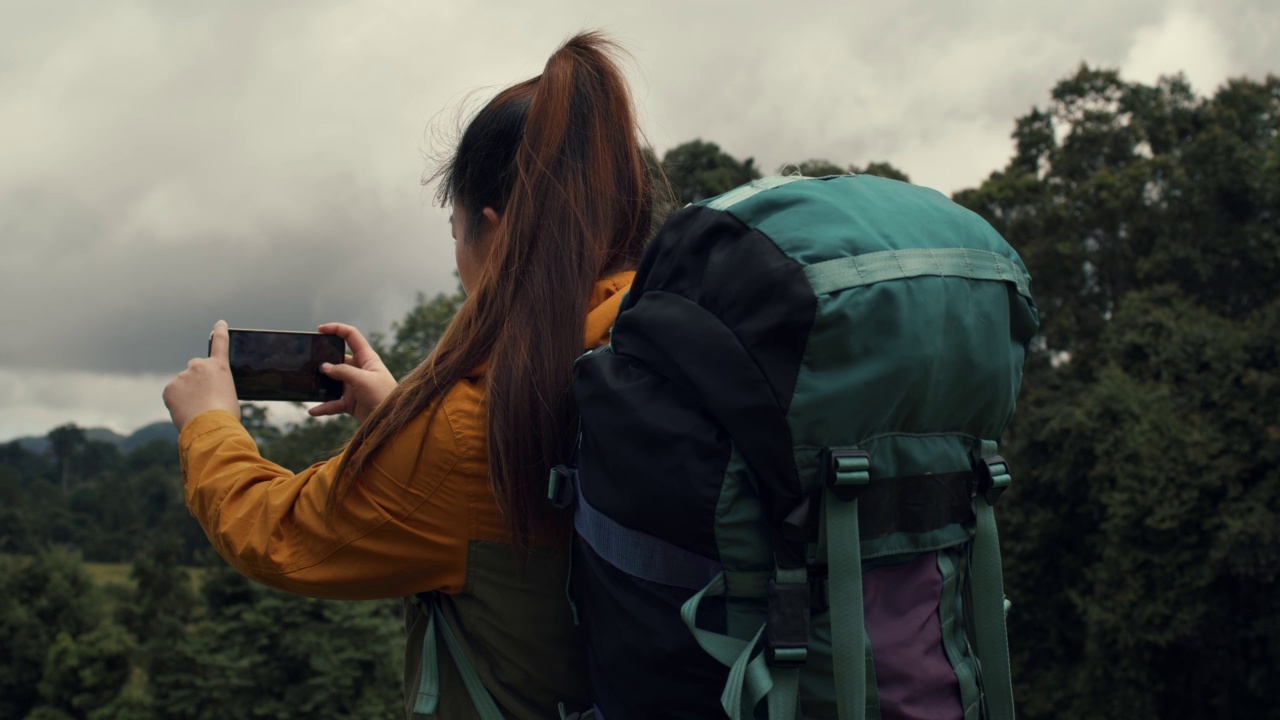 泰国森林徒步旅行的年轻女子。背着背包的活跃健康的女人。女性旅行者与漫步森林后视图，休闲，生物旅游，徒步旅行。她正在拍照。视频下载