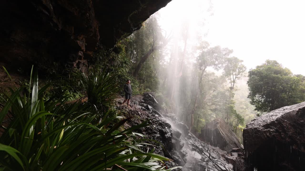 一名徒步旅行者停下脚步，用手机拍下了被雨林包围的瀑布视频素材