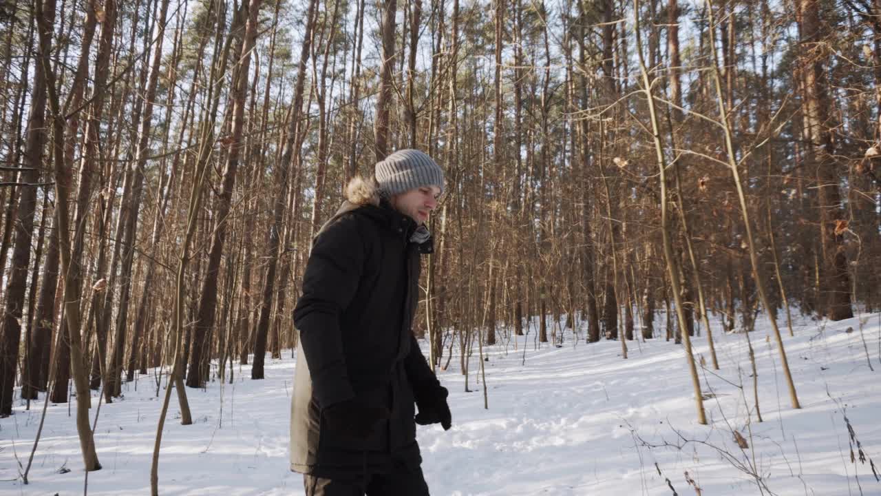 一名男子推着一个孩子，穿着暖和的夹克，坐在红色的雪橇上，穿过阳光明媚的冬季森林。视频素材