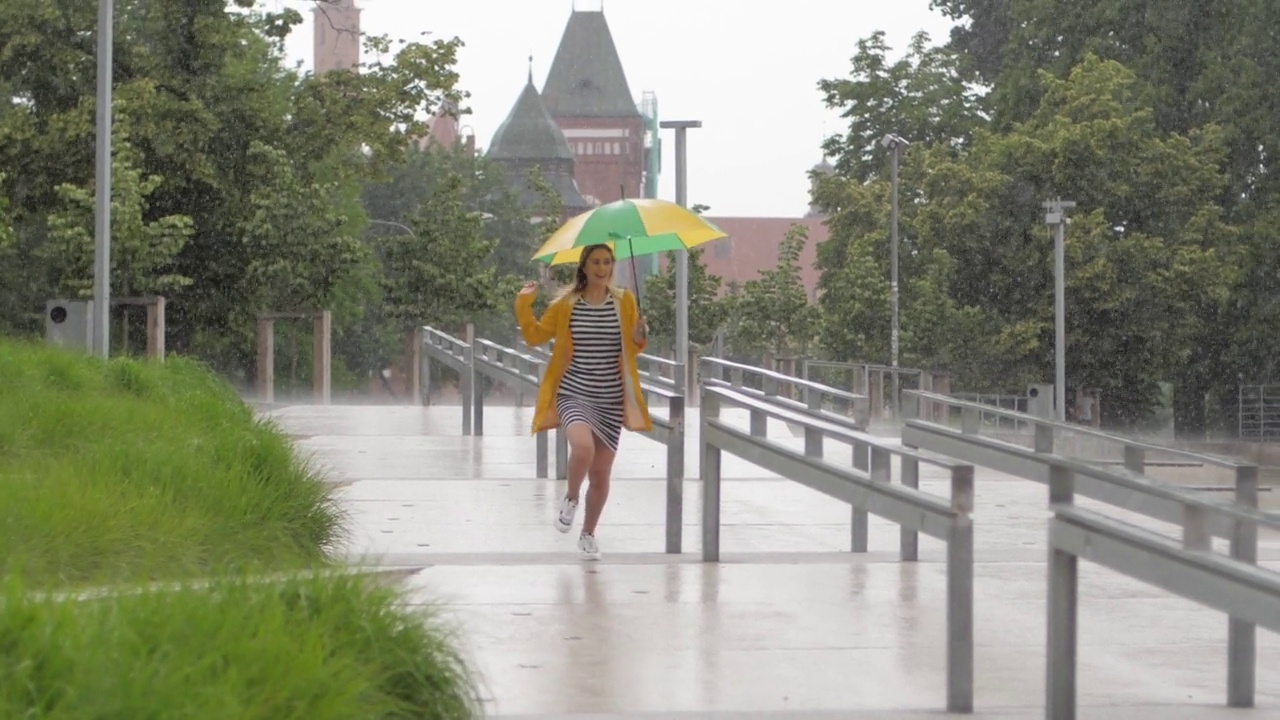 慢镜头可爱的小女孩穿着黄色雨衣撑着伞在阵雨中奔跑视频素材