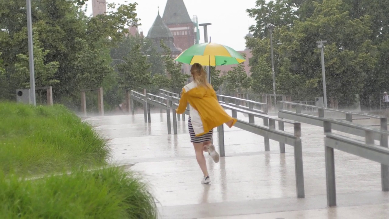 慢镜头可爱的小女孩穿着黄色雨衣撑着伞在阵雨中奔跑视频素材