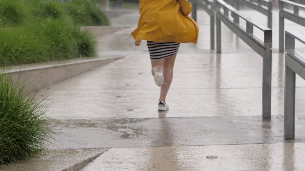 慢镜头可爱的小女孩穿着黄色雨衣撑着伞在阵雨中奔跑视频素材