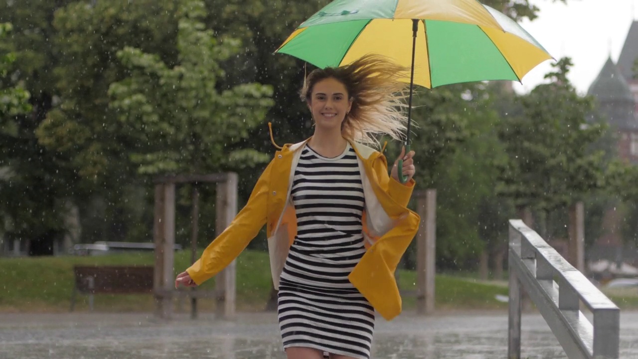 慢镜头可爱的小女孩穿着黄色雨衣撑着伞在阵雨中奔跑视频素材