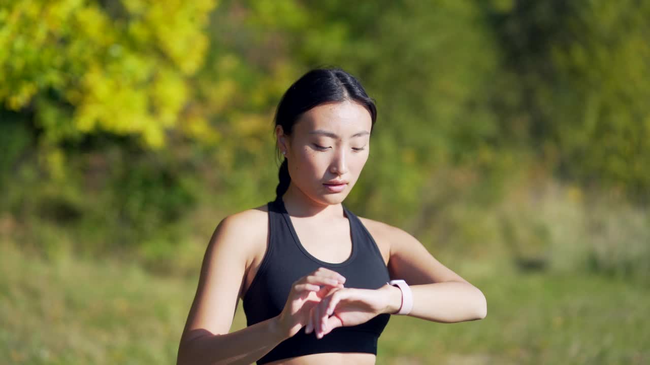 运动亚洲女性看智能手表在现代田径运动员使用使用智能手表健身手环画像视频素材