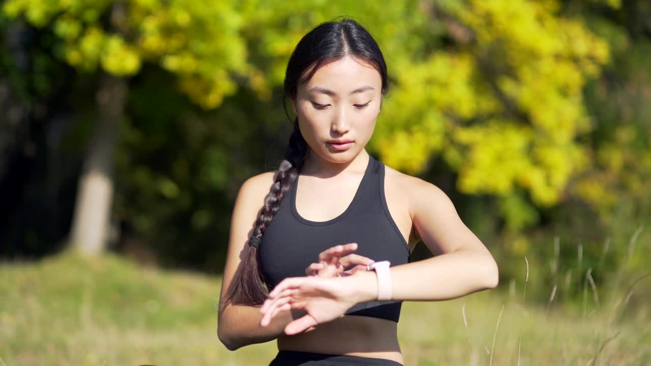 运动亚洲女性看智能手表在现代田径运动员使用使用智能手表健身手环画像视频素材