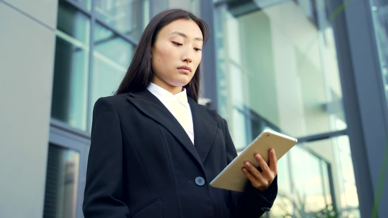 亚洲女商人在商业穿着西装站在工作与平板电脑在背景现代办公楼中心外视频素材