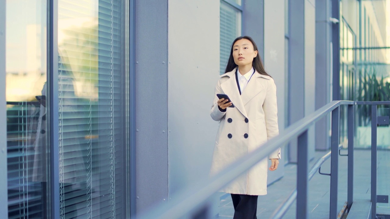 穿着西装的女商人或大学生走在城市的街道上，用手机聊天。视频素材