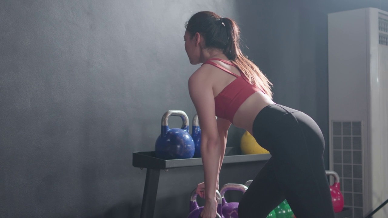 年轻的亚洲女性做训练举重壶铃侧面视图在健身房里锻炼。健身运动员漂亮的女孩穿着运动服持有壶铃。健康的生活方式的概念。视频素材