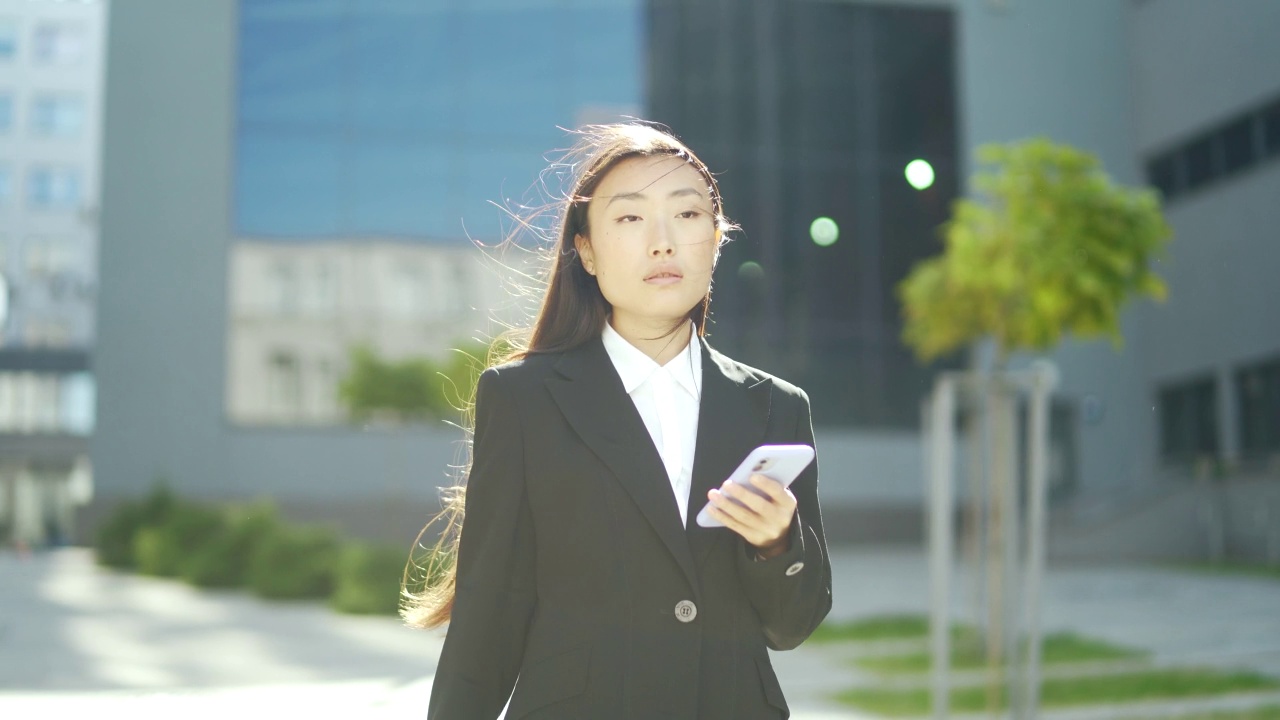 穿着西装的女商人或大学生走在城市的街道上，用手机聊天视频素材