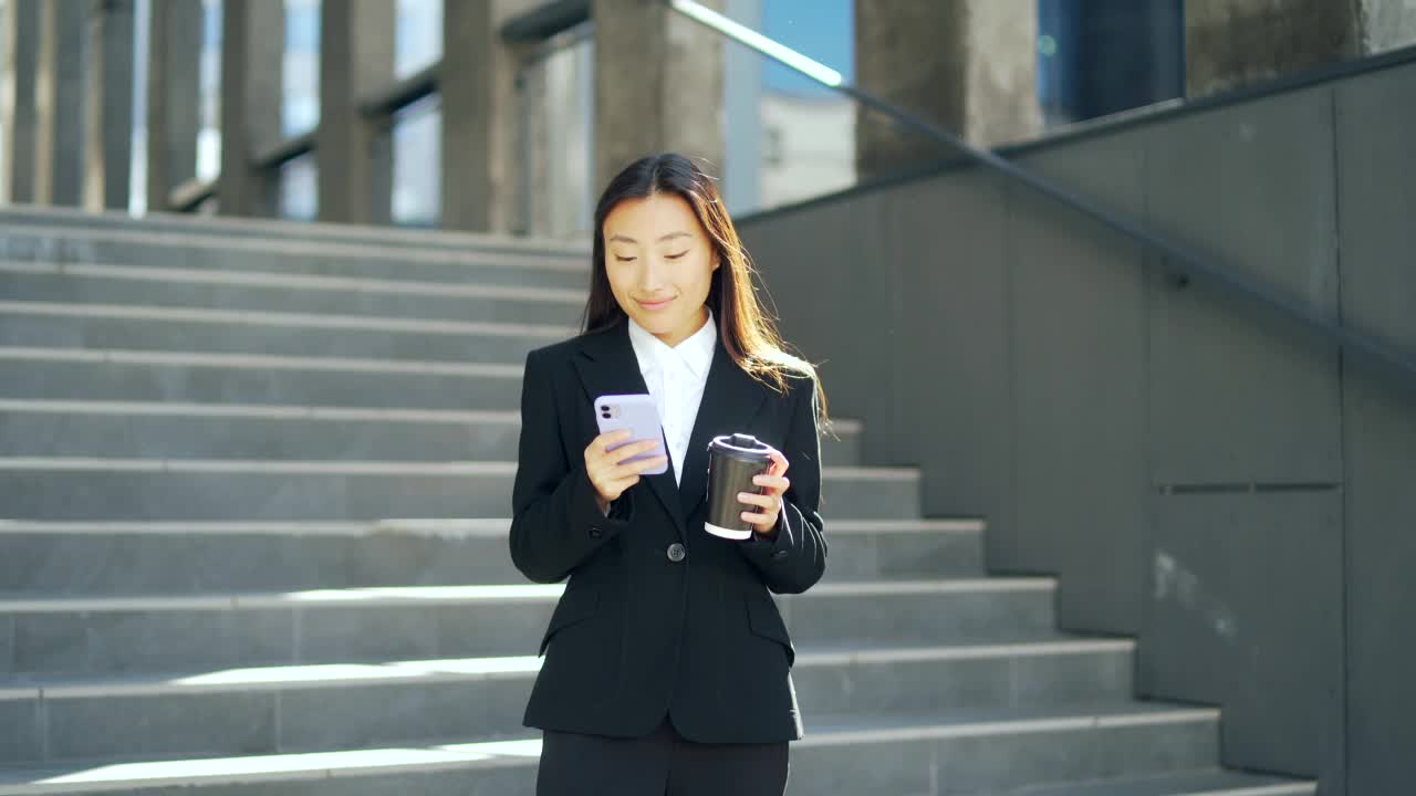 自信的经理商人走在城市街道附近的大现代商业区。年轻的亚洲女性用智能手机发短信，喝咖啡视频素材