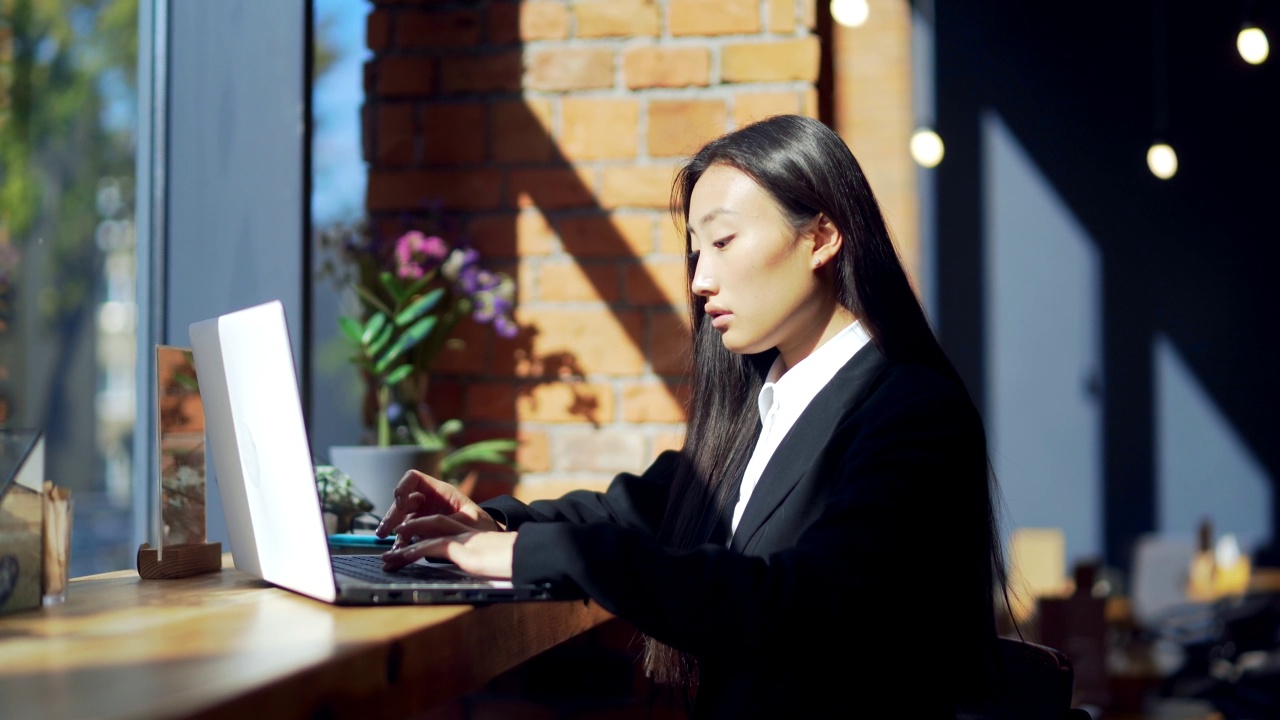 年轻的女性自由职业者或在线工作或在咖啡馆远程学习的学生。亚洲商业女性西装使用打字笔记本电脑在工作的共同工作热办公桌。视频素材