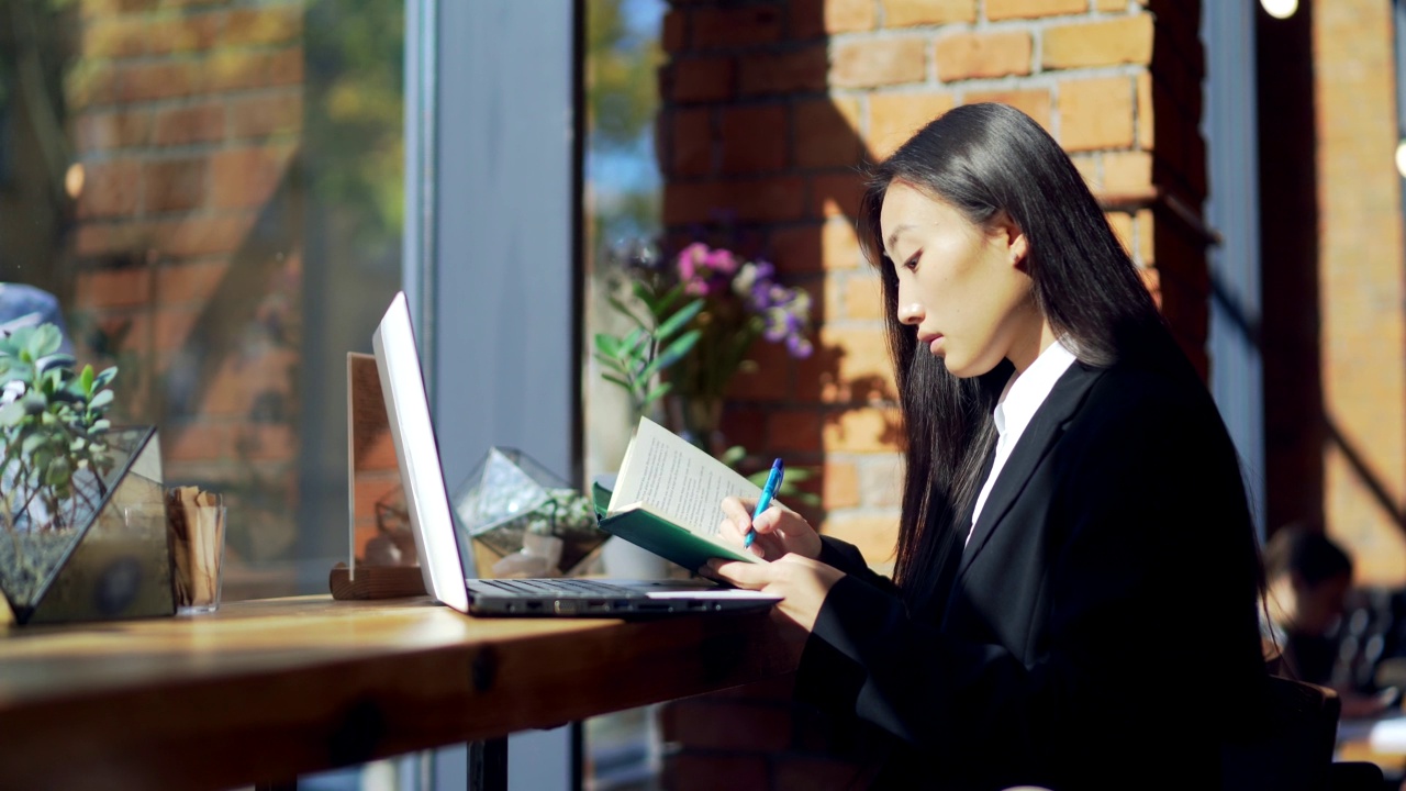 年轻的女性自由职业者或在线工作或在咖啡馆远程学习的学生。亚洲商业女性西装使用打字笔记本电脑在工作的共同工作热办公桌视频素材