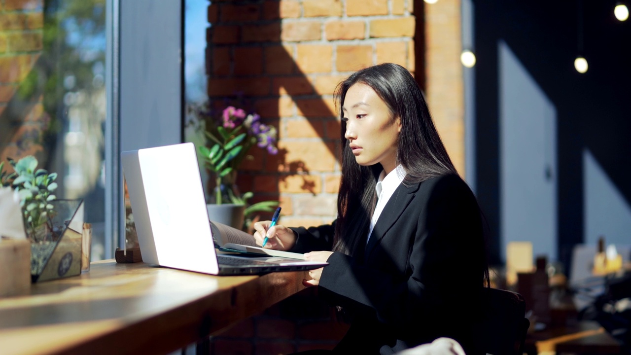 年轻的女性自由职业者或在线工作或在咖啡馆远程学习的学生。亚洲商业女性西装使用打字笔记本电脑在工作的共同工作热办公桌。视频素材