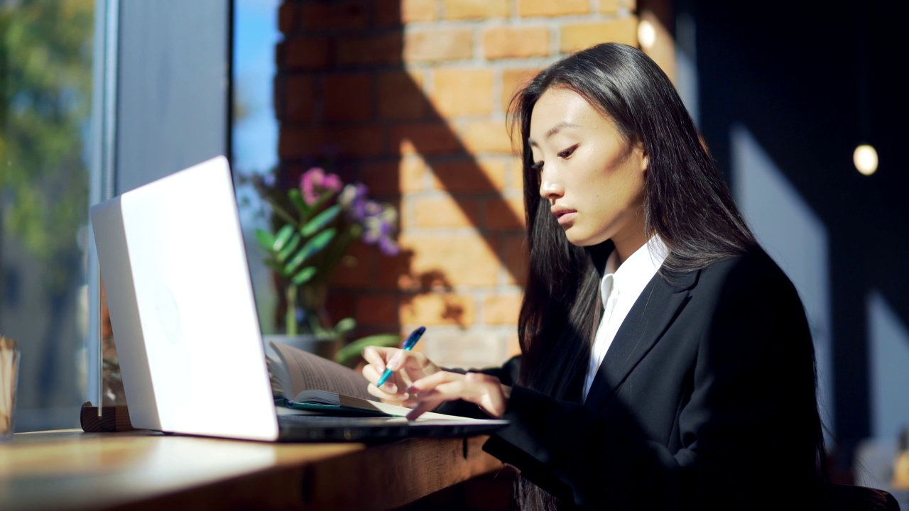 年轻的女性自由职业者或在线工作或在咖啡馆远程学习的学生。亚洲商业女性西装使用打字笔记本电脑在工作的共同工作热办公桌视频素材