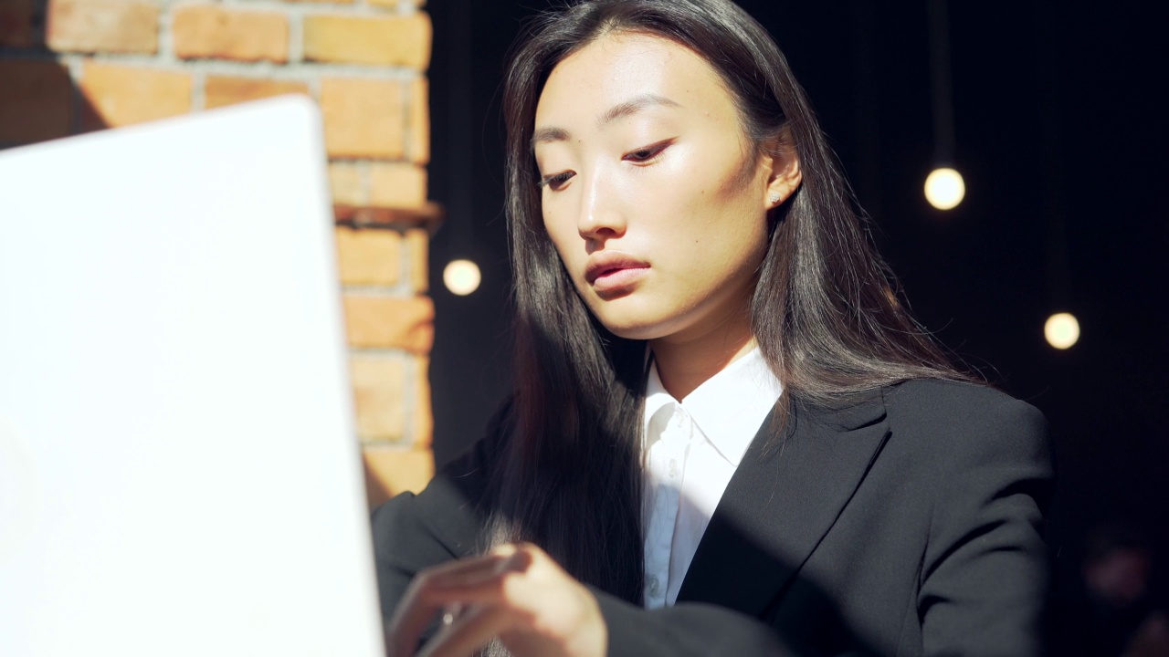 年轻的女性自由职业者或在线工作或在咖啡馆远程学习的学生。亚洲商业女性西装使用打字笔记本电脑在工作的共同工作热办公桌。视频素材