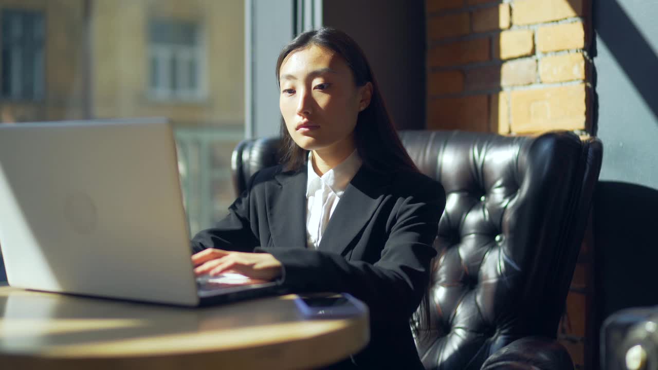 年轻的女性自由职业者或在线工作或在咖啡馆远程学习的学生。亚洲商业女性西装使用打字笔记本电脑在工作的共同工作热办公桌。视频素材