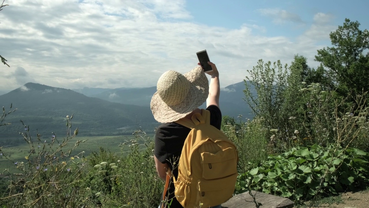 女旅游博主在绿色风景的山顶上用手机自拍视频素材