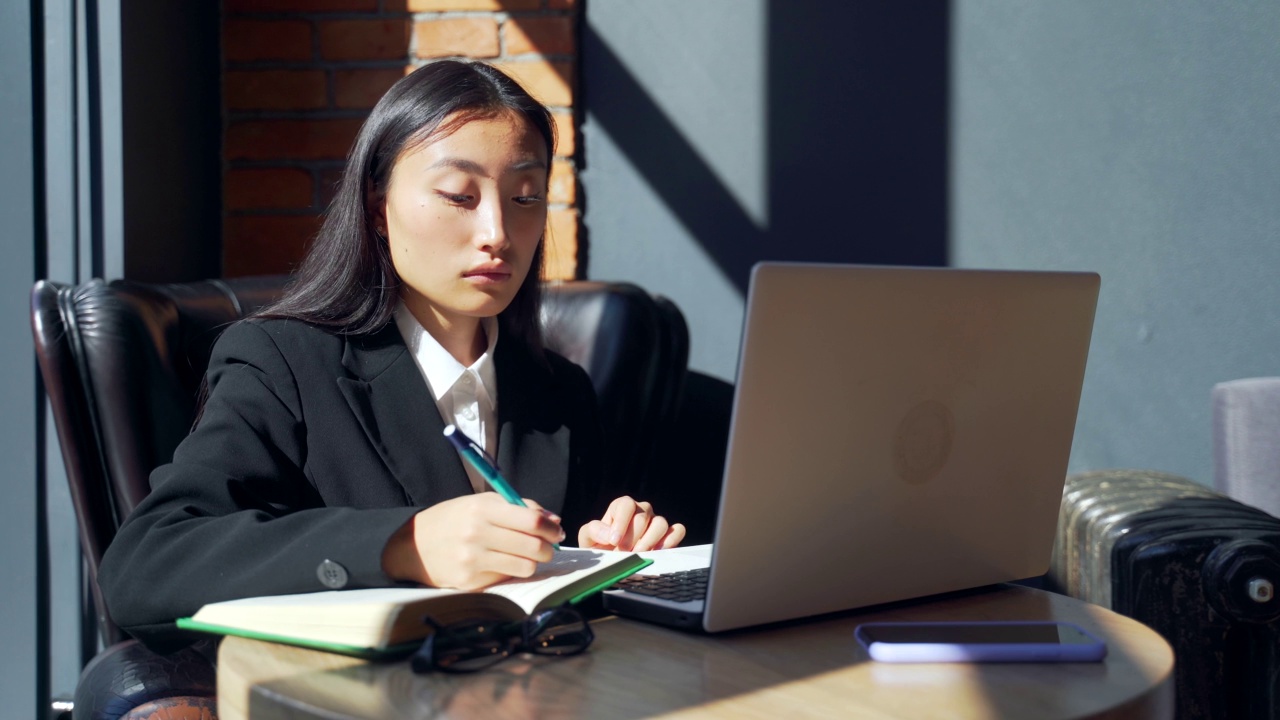 年轻的女性自由职业者或在线工作或在咖啡馆远程学习的学生。亚洲商业女性西装使用打字笔记本电脑在工作的共同工作热办公桌视频素材