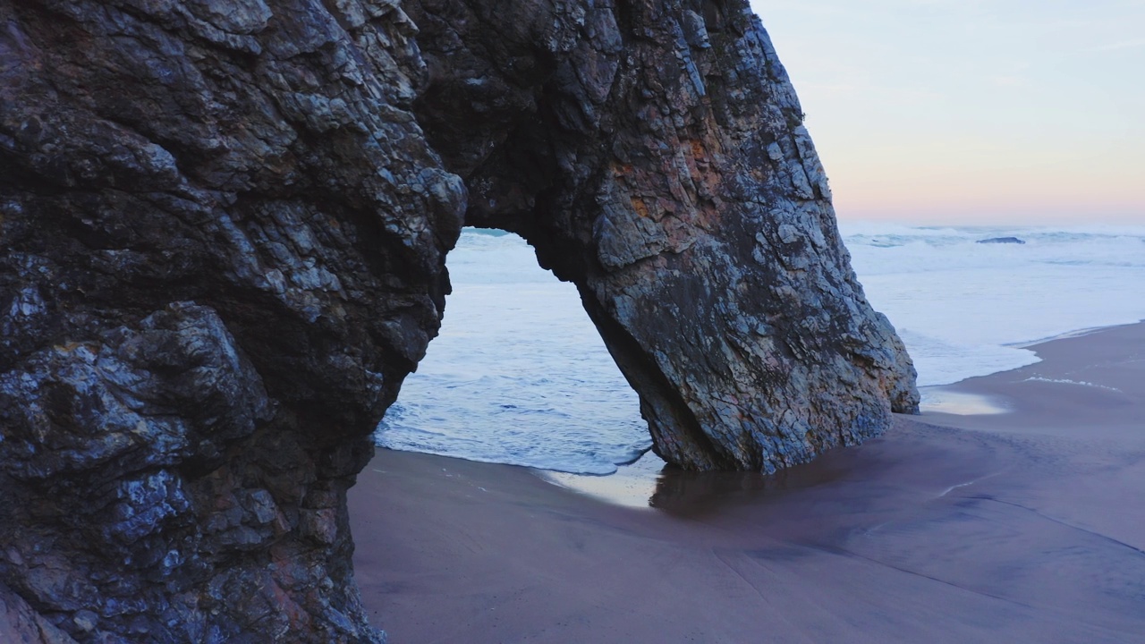 在葡萄牙海岸，由辛特拉(Sintra)在普拉亚达阿德拉加(Praia da Adraga)拍摄的拱形岩石形成的里斯本海滩的无人机视图视频素材