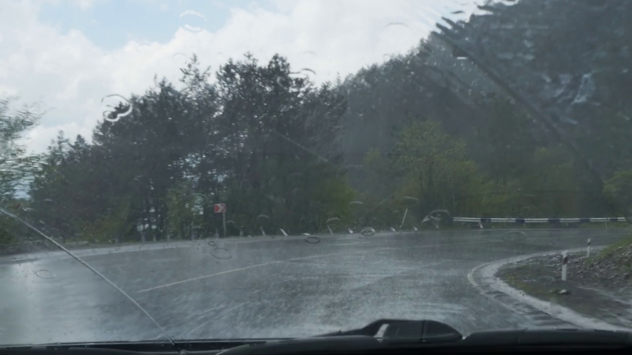 当汽车行驶在山路上时，大雨滴在汽车的挡风玻璃上。雨刷用于清除挡风玻璃上的水视频素材