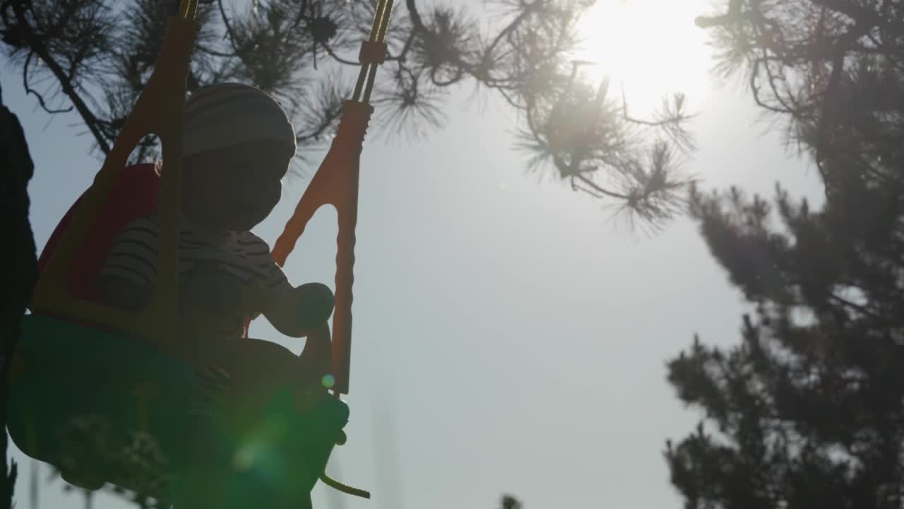 一个阳光明媚的夏天，孩子们在户外玩秋千，秋千挂在树上，一个宝宝在阳光下摆动的剪影。儿童健康的夏季活动。视频素材