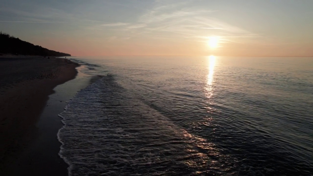 夕阳下空旷的海滩，无人机在水面上飞行，反射出天空的橙色。视频素材