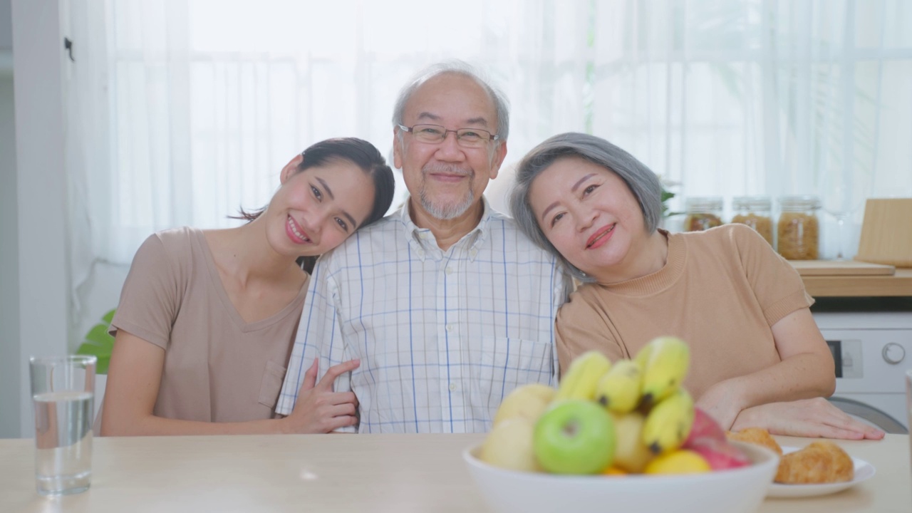 亚洲老年夫妇与年幼的女儿坐在房子里的肖像。迷人美丽的孙女探望年迈成熟的祖父母，然后微笑着，在家里的客厅一起看镜头视频素材