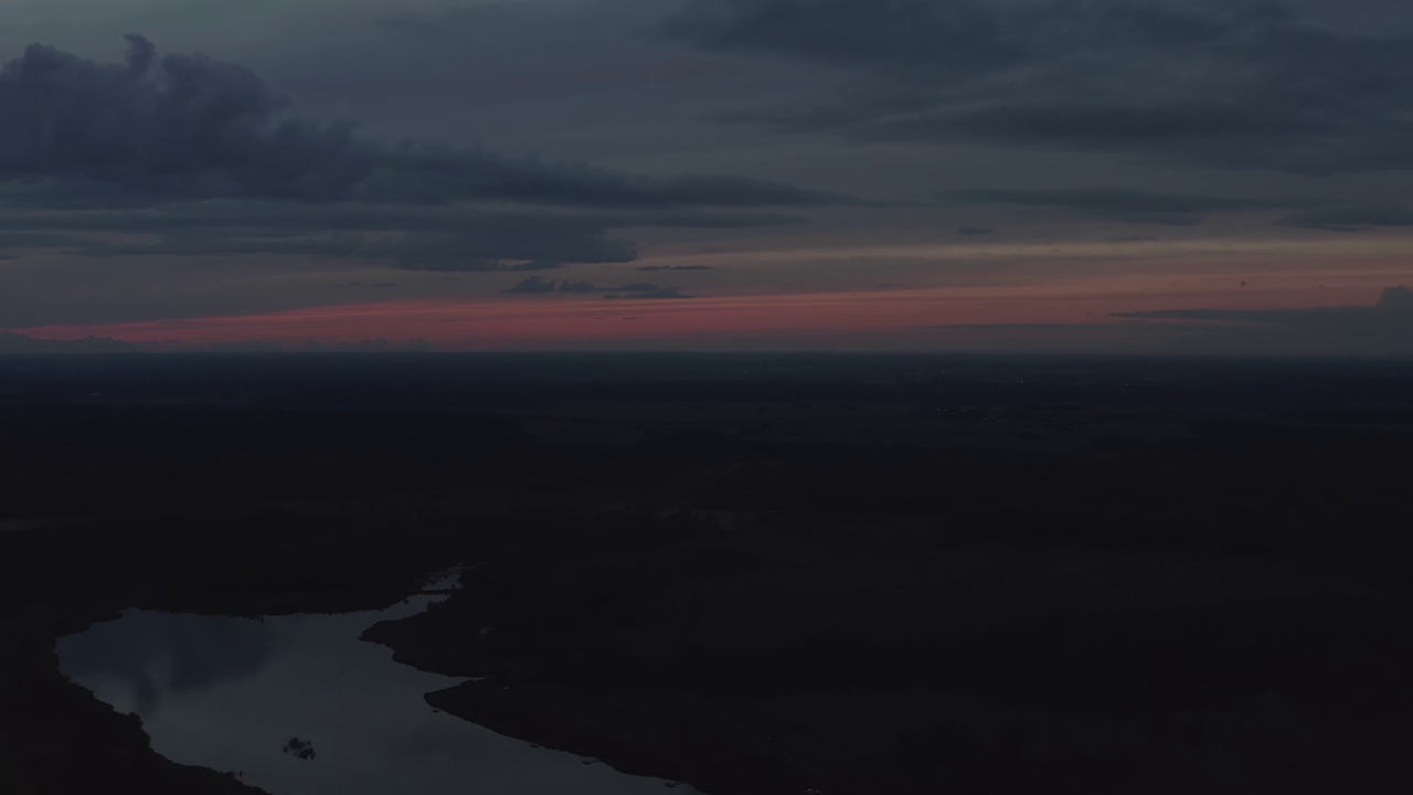 无人机视频。在夏天。夕阳西下，夜晚红彤彤的天空，笼罩着森林中的一个湖泊视频素材