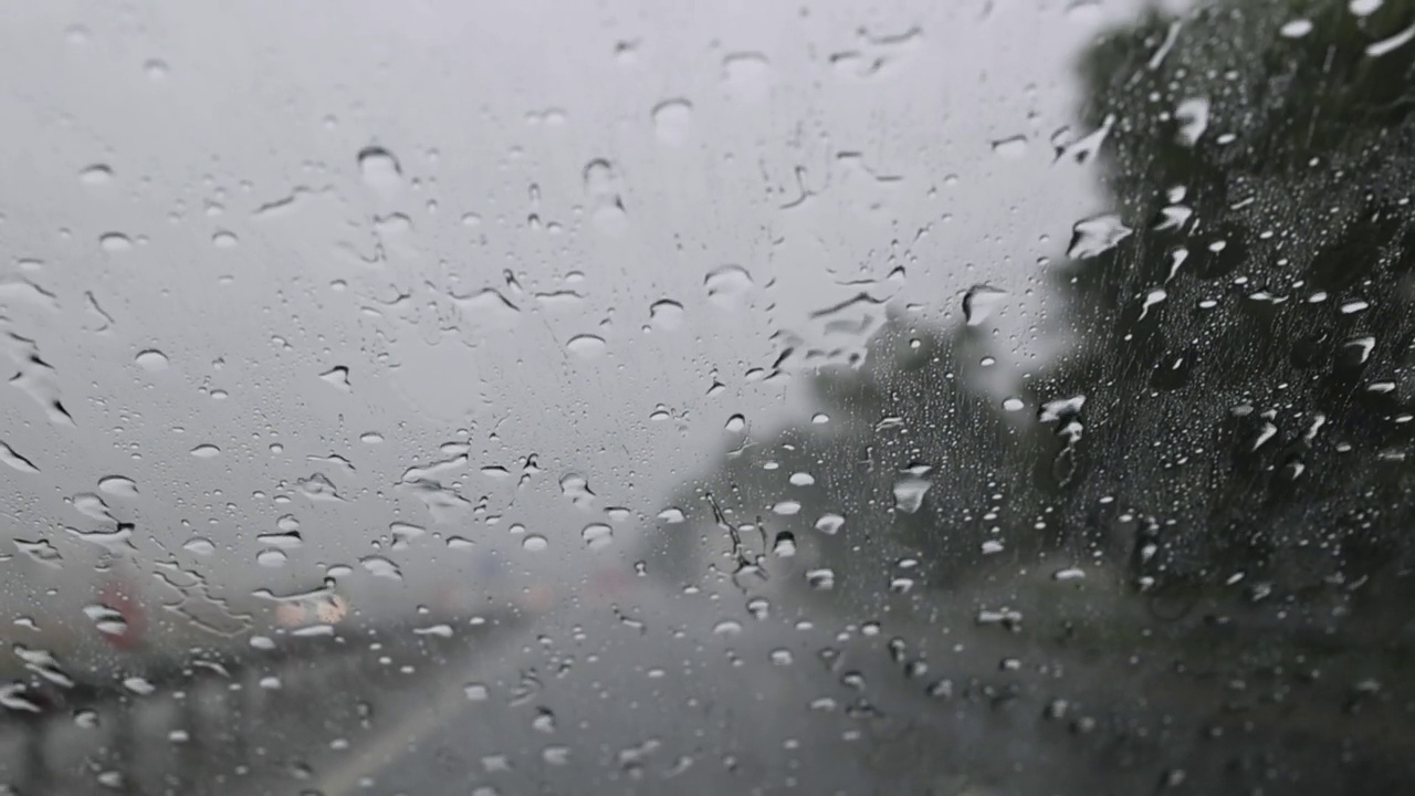 雨水落在用防水蜡处理过的汽车挡风玻璃上。在倾盆大雨中在高速公路上开车，开着车，迎面而来的车前灯模糊视频素材