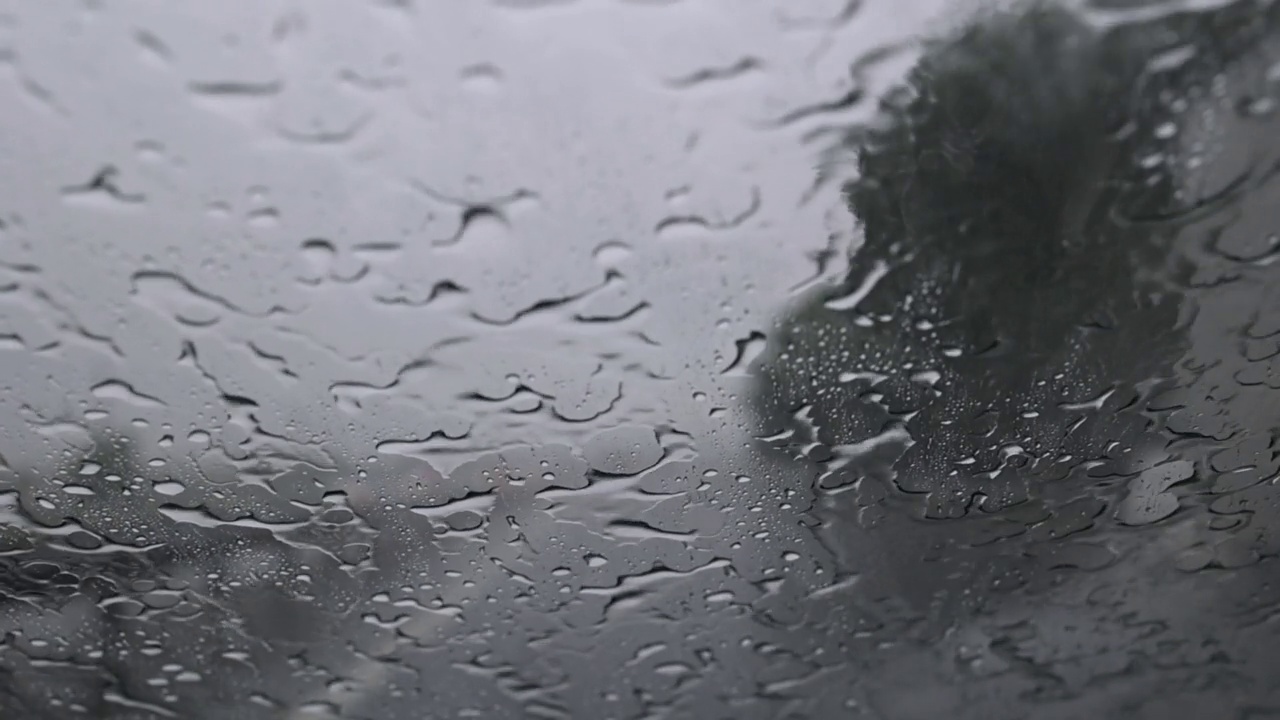 雨水落在用防水蜡处理过的汽车挡风玻璃上。在倾盆大雨中在高速公路上开车，开着车，迎面而来的车前灯模糊视频下载