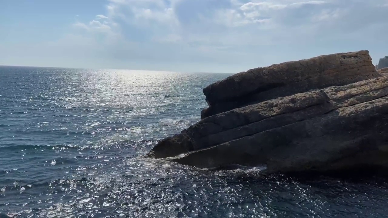 闪闪发光的蓝色银色海浪的岩石海岸线。夏日海面上美丽的云朵。视频素材